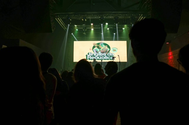 Silhuetas do público contra o telão verde do Jingles da República.